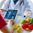 Nutritionist female doctor using digital mobile tablet with virtual graphic icon diagram and vegetable and fruit with patient on desk at office hospita